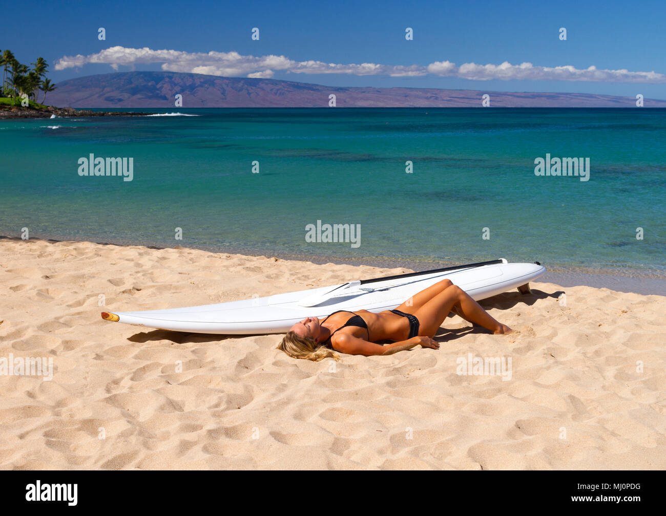 Femme en bonne santé se détend sur plage avec paddleboard standup à Napili Bay, Maui, Hawaii. L'île de Lanai peut être vu dans la distance. Banque D'Images