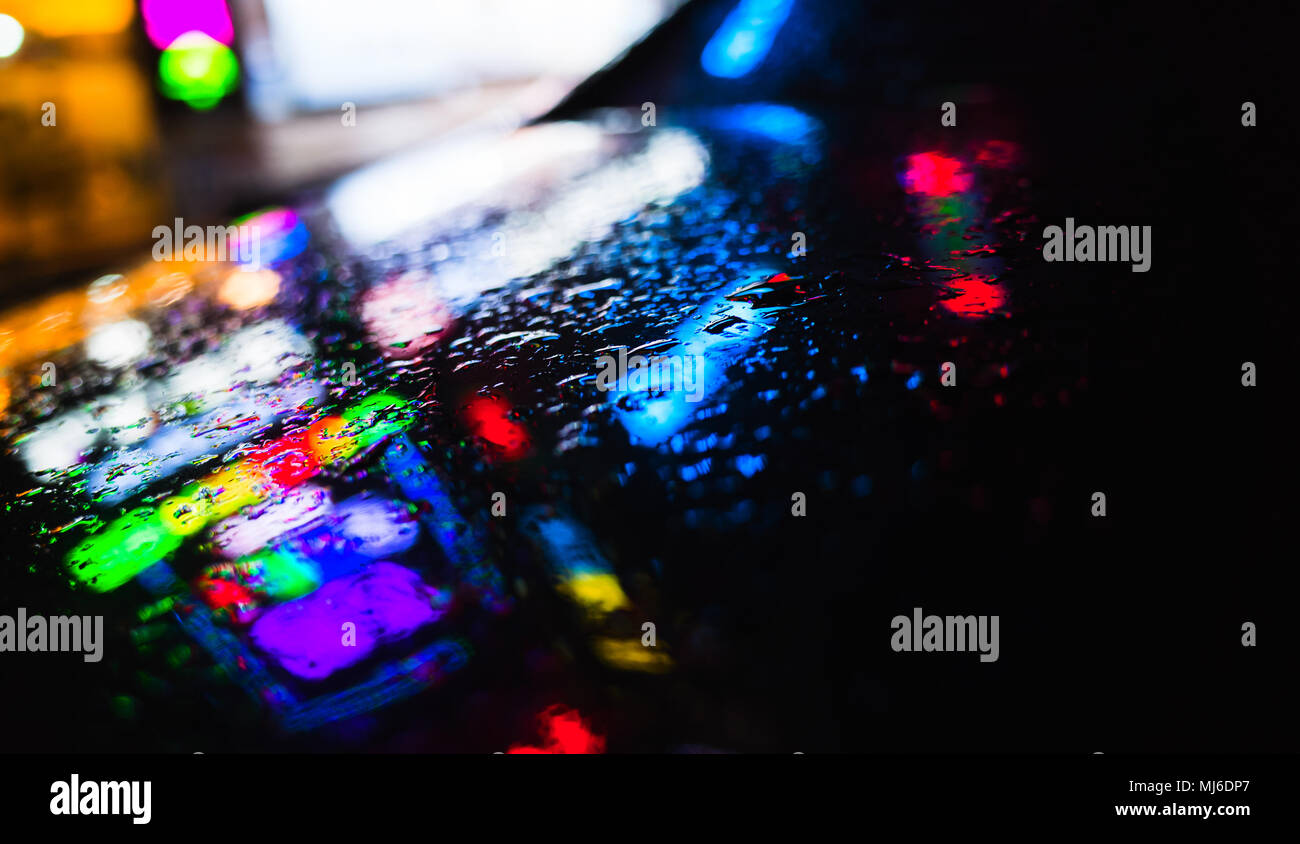 Résumé nuit ville fond flou coloré, réflexions sur un capot de voiture humide noir Banque D'Images
