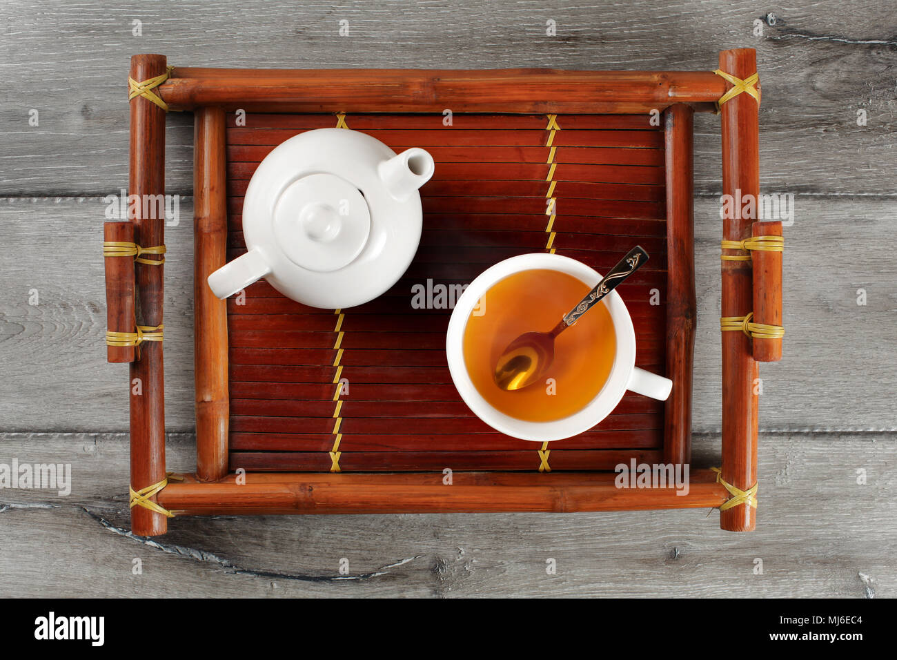 Vue de dessus de table en bois de bambou sur plateau avec petite théière en céramique et d'un plateau tasse pleine de thé noir à la vapeur chaude et cuillère en argent. Banque D'Images