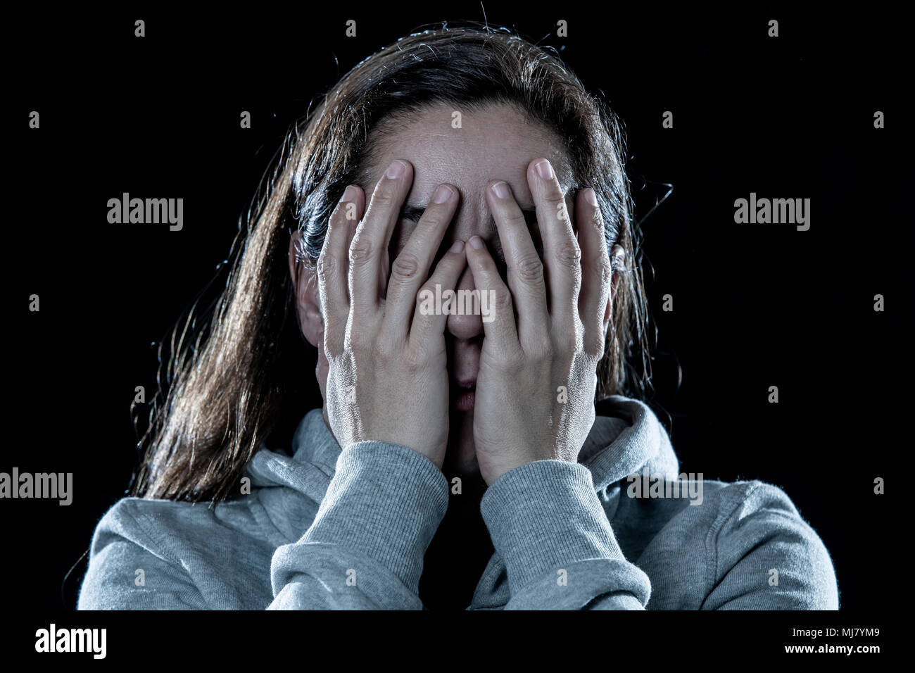 Concept de la peur, la honte, la violence et la dépression. L'attrayant enfoncée femme couvre son visage avec ses mains sur un fond noir isolé Banque D'Images
