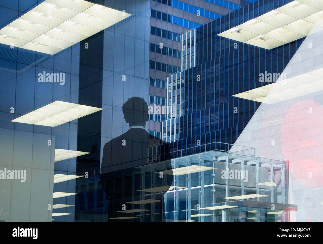 Vue arrière d'un homme portant costume standing at window, réflexions de bureau encastré plafonniers et gratte-ciel. Banque D'Images