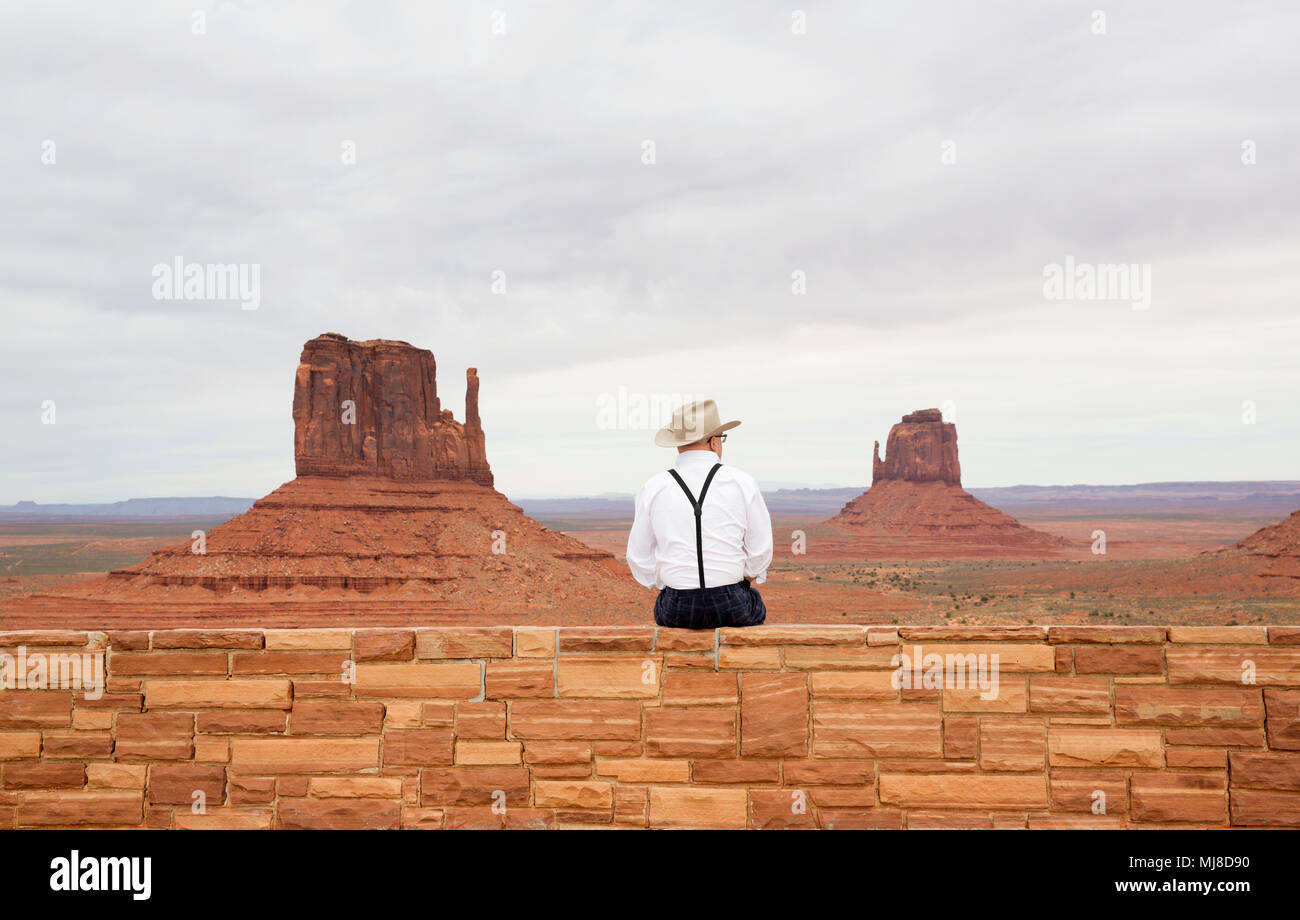 Vue arrière de man wearing cowboy hat, assis sur le mur de pierre, à la formations de roche au canyon. Banque D'Images