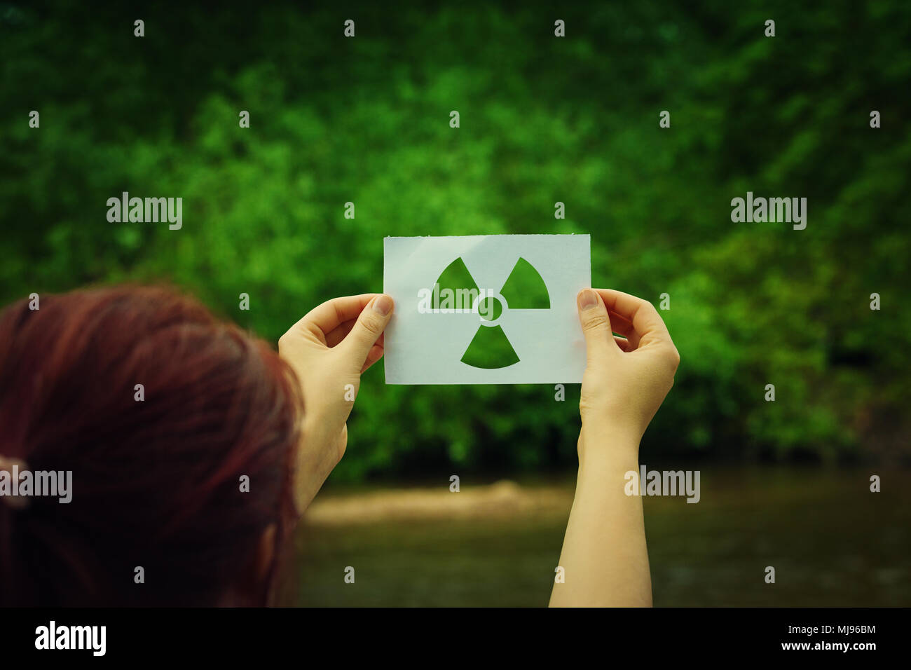 Femme tenant une feuille de papier avec symbole symbole de rayonnement sur fond vert de la forêt. Problèmes de l'environnement concept, comme danger de catastrophe radioactive Banque D'Images