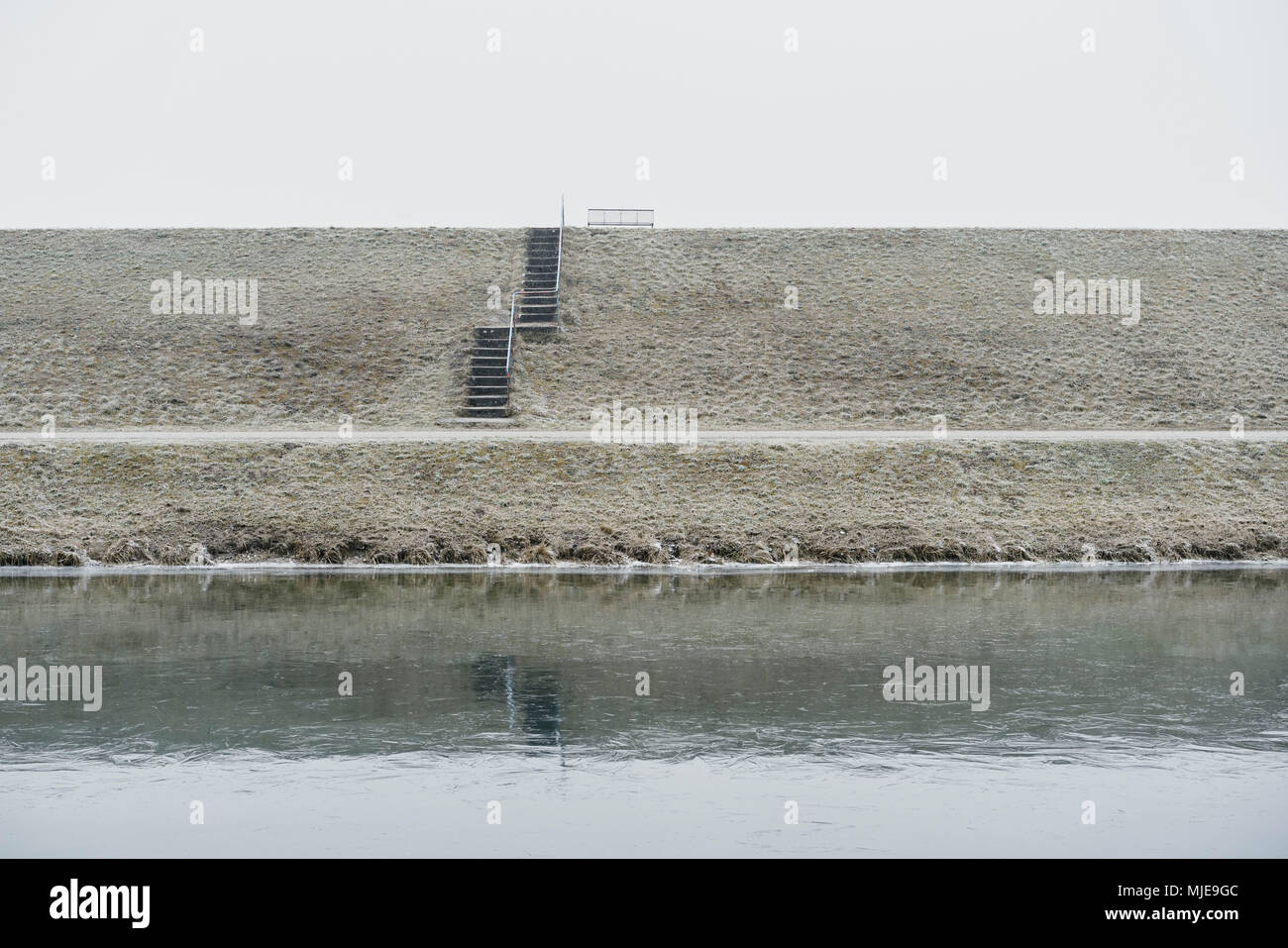 Banc en métal sur une digue avec des escaliers, de l'hiver, ciel gris blanc, eaux en premier plan Banque D'Images