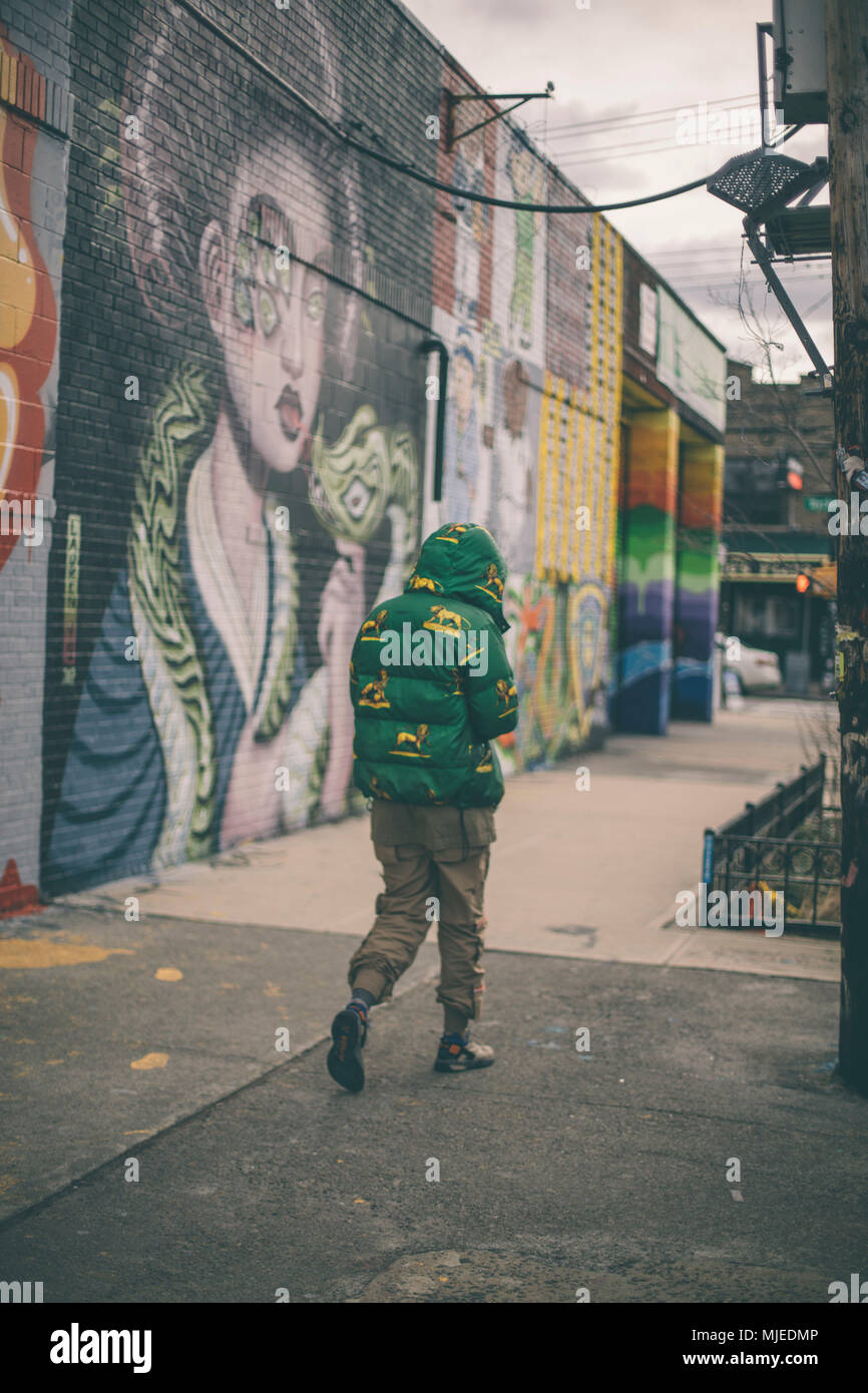 Jeune homme marchant avec un manteau vert sur Bushwick zone graffiti. Banque D'Images