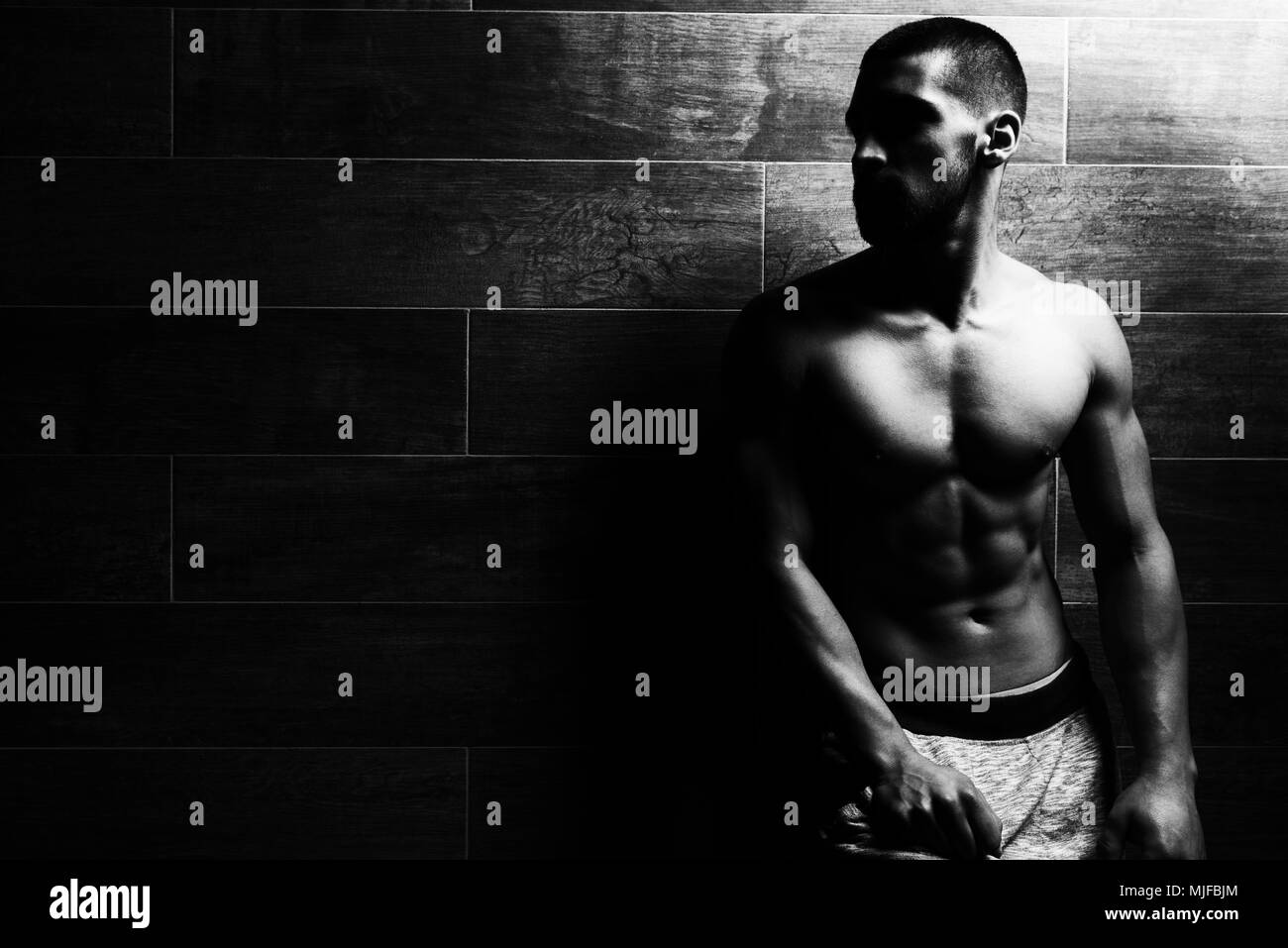 Jeune homme sain Soyons forts adossée au mur et Flexing Muscles - Remise en forme musculaire Bodybuilder Athletic Model Posing après exercices - un Banque D'Images