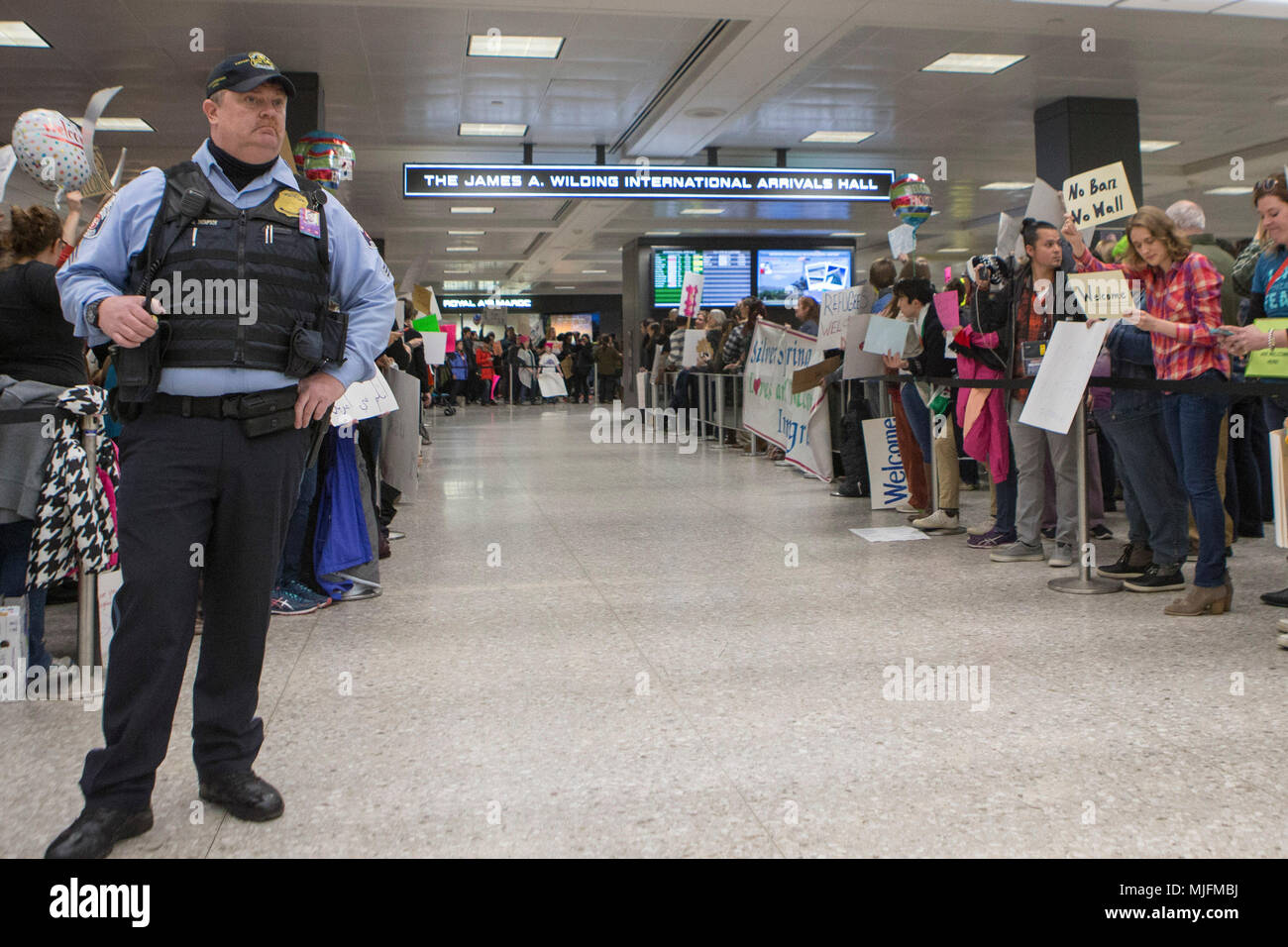 Un policier monte la garde comme ligne de manifestants la zone de sortie des douanes des États-Unis au cours d'un rassemblement contre le Président Donald J. Trump a proposé l'interdiction de voyager visant les pays majoritairement musulmans détenus à l'extérieur de la sortie de la douane américaine au terminal des arrivées internationales de l'Aéroport International de Dulles, le 28 janvier 2017 à Dulles, Virginie. Banque D'Images