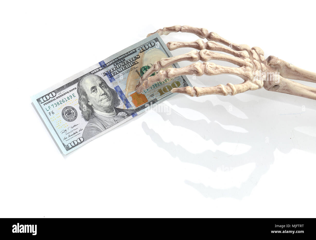 Skeleton hand holding a 100 US dollar bank note sur blanc. Banque D'Images