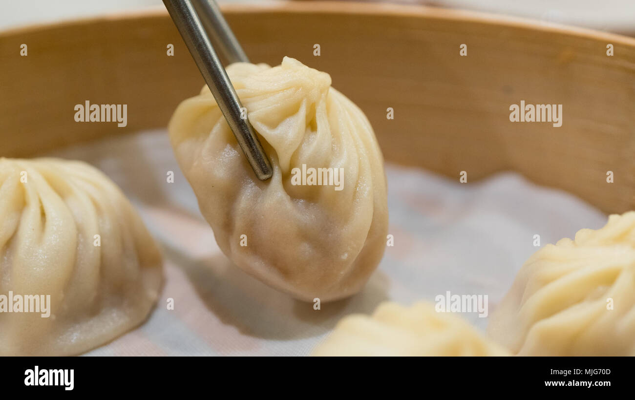 Baguettes de prendre une boulette de porc Xiaolongbao taiwanais dans un panier de bambou Banque D'Images