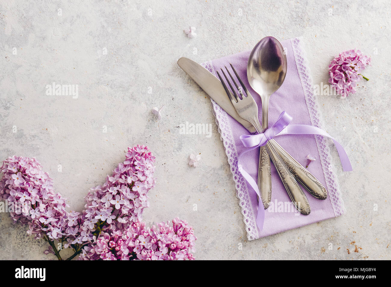 Décoration de table de printemps avec des fleurs lilas. Table élégante avec des fleurs lilas mauve, serviette et argenterie vintage sur fond rustique. Banque D'Images