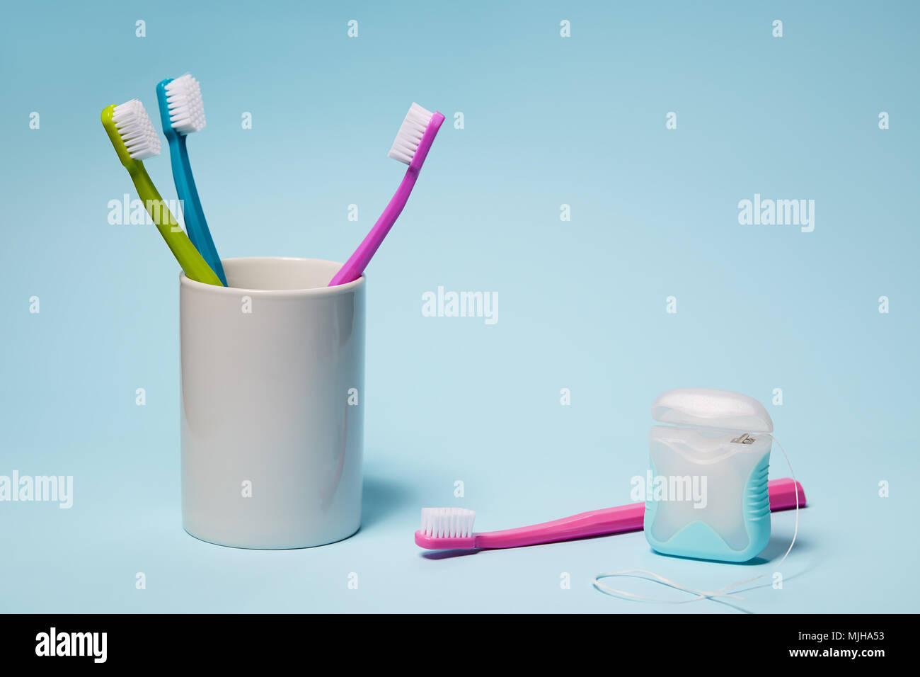 L'équipement dentaire. Brosses à dents colorées dans la tasse et du fil dentaire sur fond bleu clair. L'espace de copie, studio shot. Banque D'Images