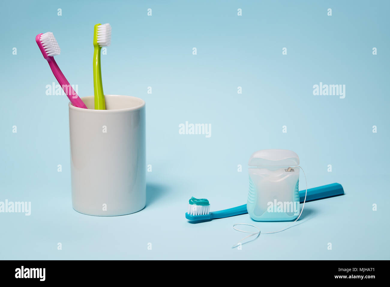 L'équipement dentaire. Brosses à dents colorées dans la tasse et du fil dentaire sur fond bleu clair. L'espace de copie, studio shot. Banque D'Images