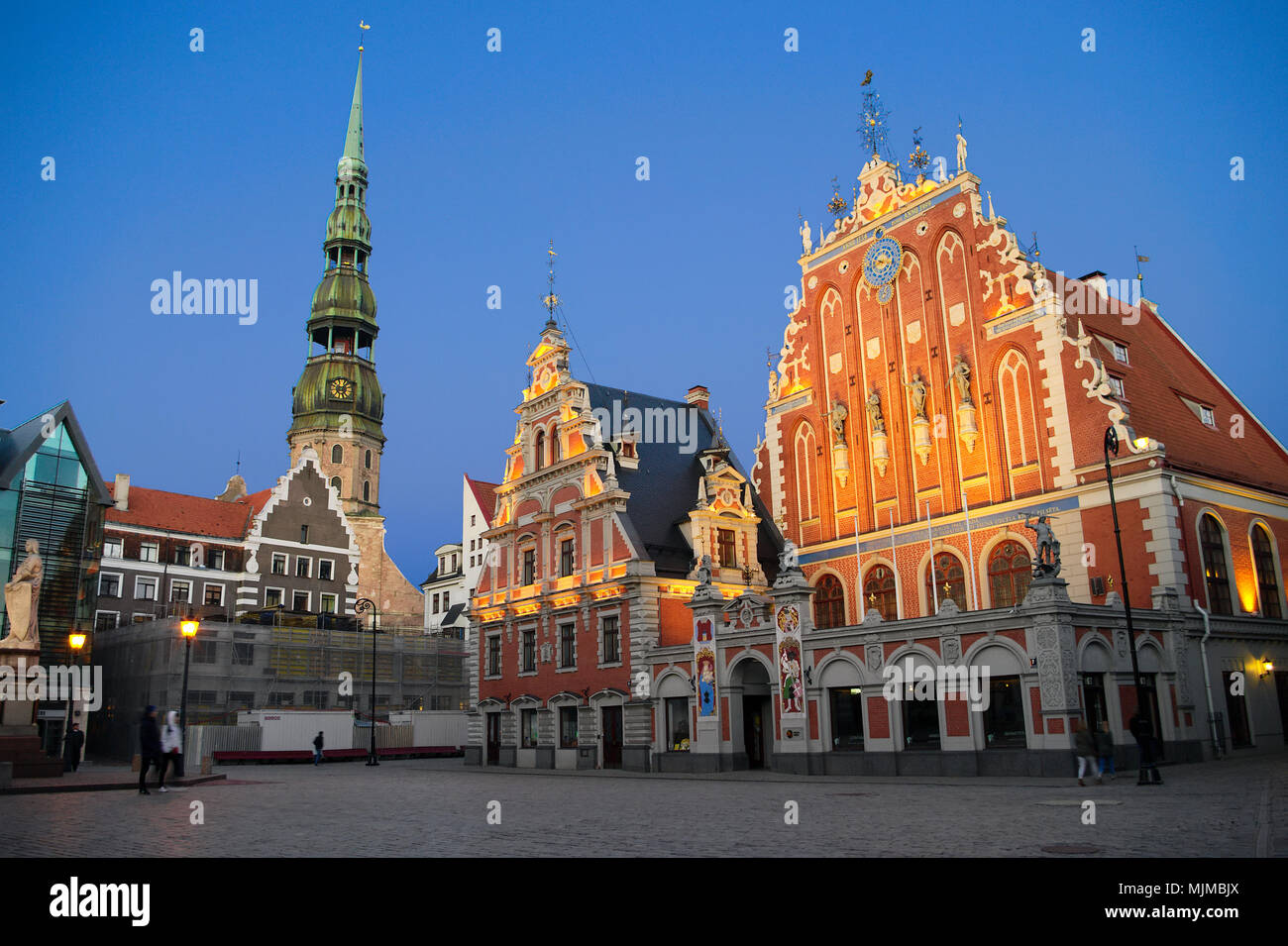 Riga, Lettonie. Maison des Têtes Noires, Melngalvju nams, avec vue sur la tour de l'Eglise Saint-Pierre de Riga. Nuit paysage urbain de la vieille ville de Riga. Banque D'Images