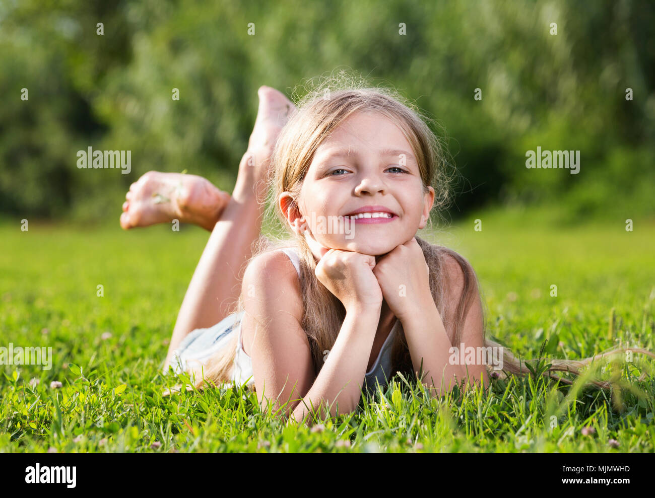 Heureuse petite fille à l'école élémentaire âge allongé sur l'herbe verte dans le parc Banque D'Images