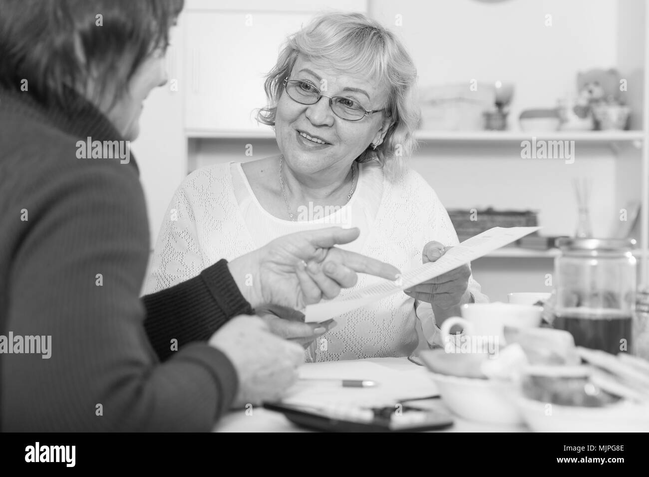 Deux femmes matures positifs considérant papers while sitting on cuisine Banque D'Images