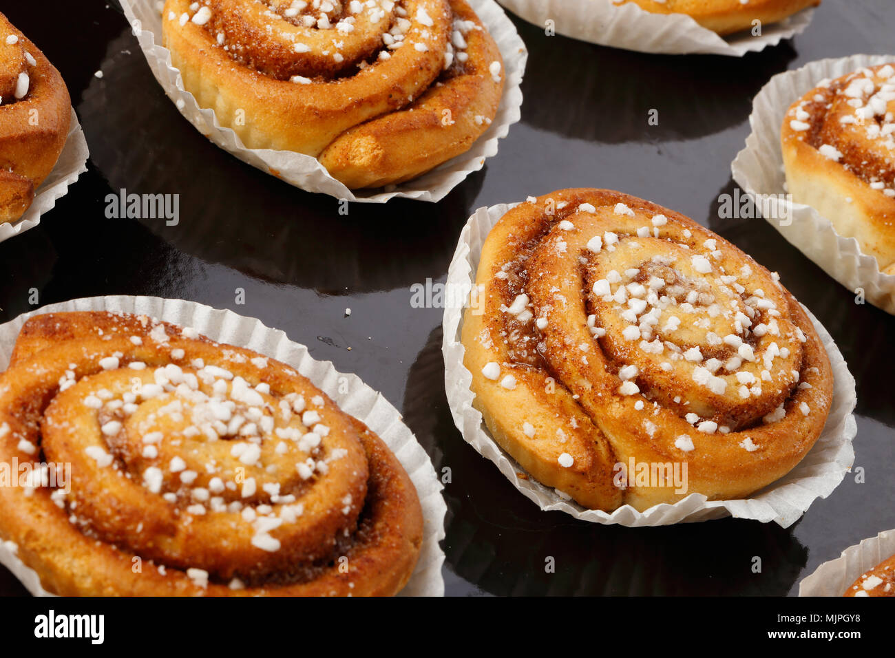 Close-up de brioches à la cannelle cuit dans des boîtes de papier graeseproof sur une plaque de cuisson. Banque D'Images