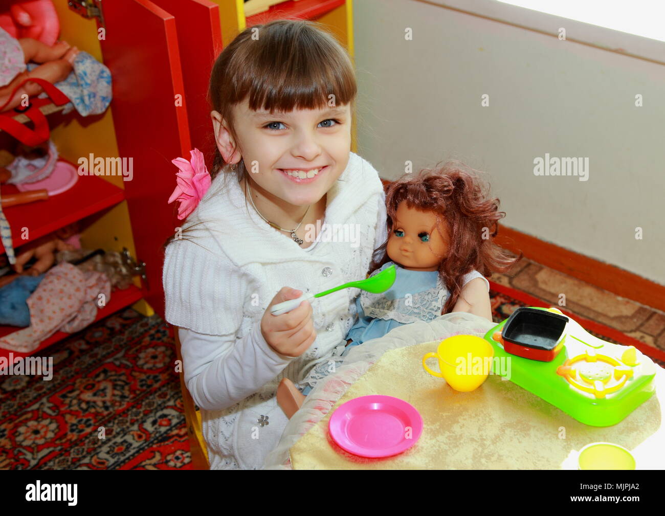 Portrait d'une belle jeune fille jouant avec une poupée. L'enfant se nourrit la poupée en maternelle. Banque D'Images