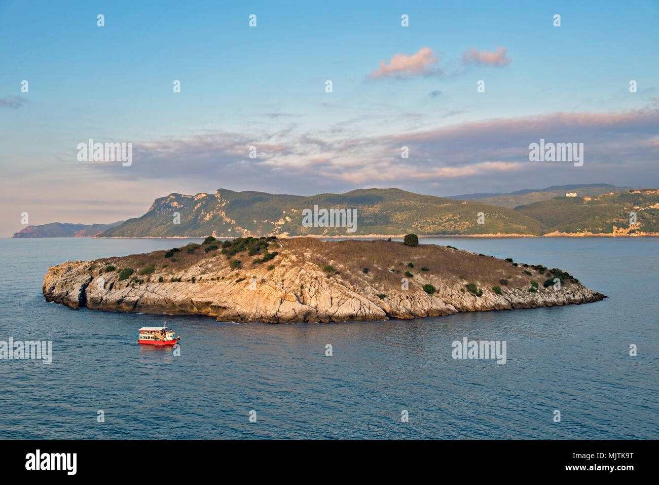 Une petite île rocheuse de tavsan entourée d'eaux bleues calmes au coucher du soleil, avec un bateau rouge. Côte de la mer Noire en Turquie, Amasra, Banque D'Images