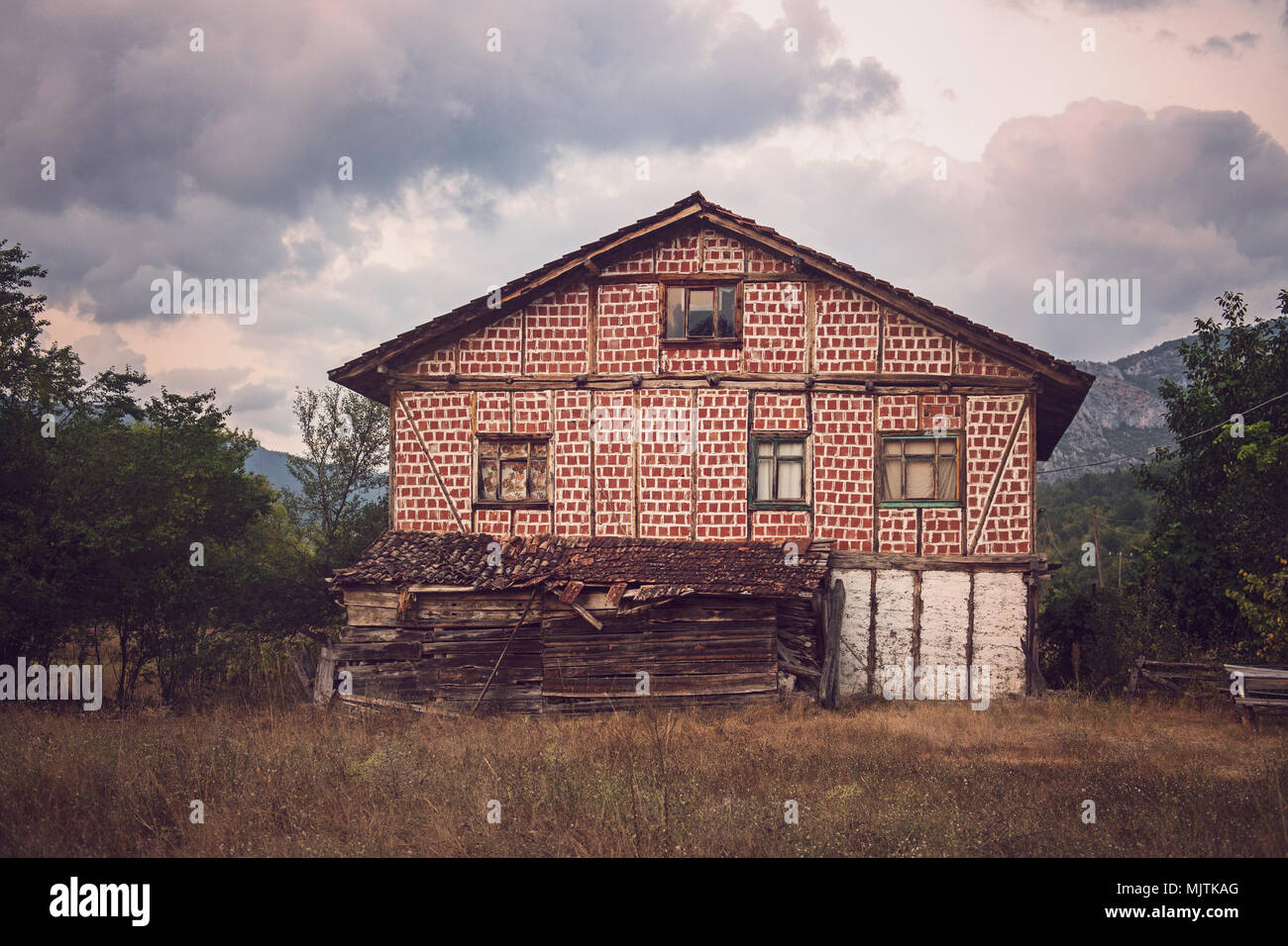 Une maison rustique abandonnée dans un cadre rural avec une façade à damiers rouge et blanc, de vieilles poutres en bois et un toit en décomposition, Banque D'Images