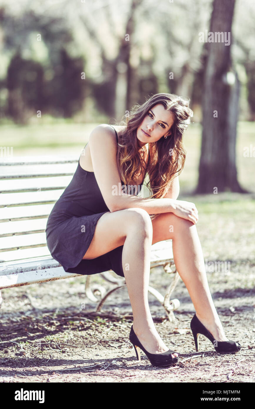 Portrait d'une jolie femme assise dans un banc dans un parc urbain portant  robe noire et talons hauts Photo Stock - Alamy