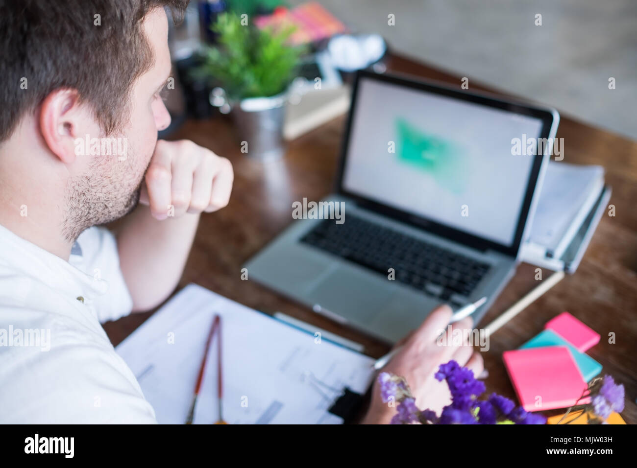 Caucasian man working on laptop assis à sa place de bureau moderne. Concept de jeunes utilisant lieu de coworking. Attendre le chargement de l'ordinateur portable. Banque D'Images