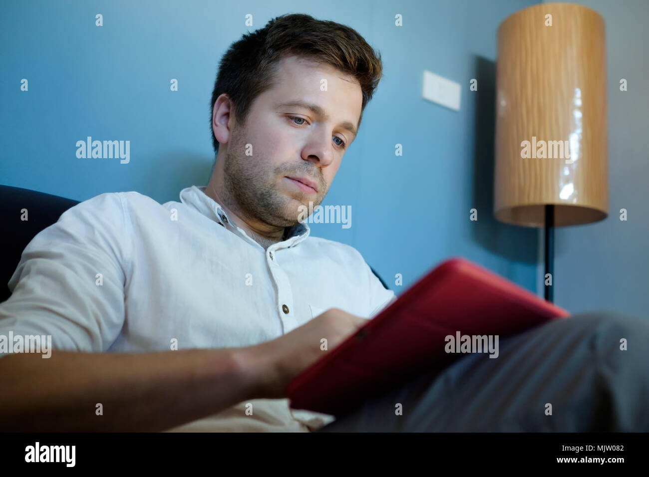 Handsome man en chemise blanche en utilisant sa tablette sitting on a couch Banque D'Images