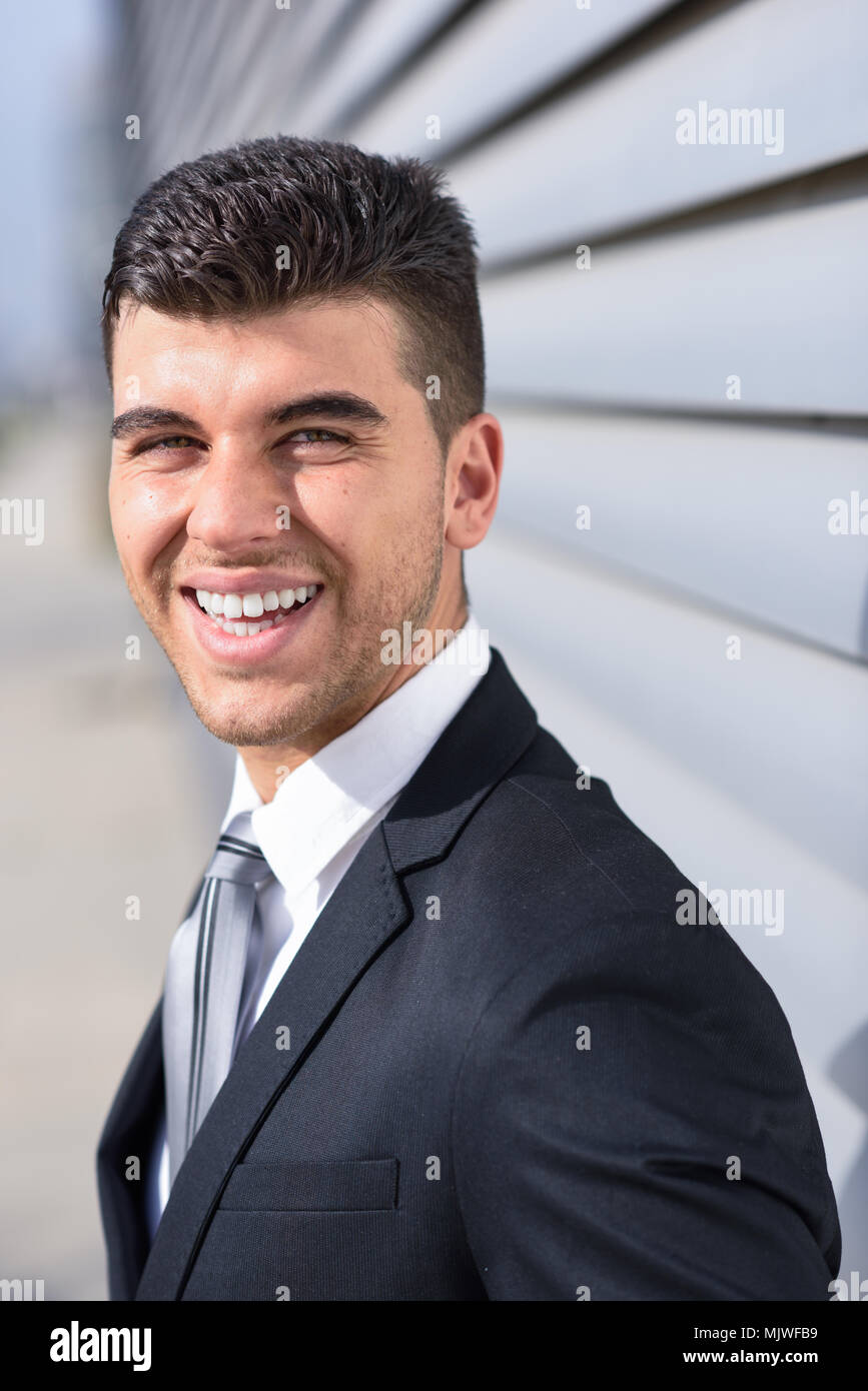 Jeune homme d'affaires à proximité d'un immeuble de bureaux modernes portant costume noir et cravate. L'homme aux yeux bleus en souriant. Banque D'Images