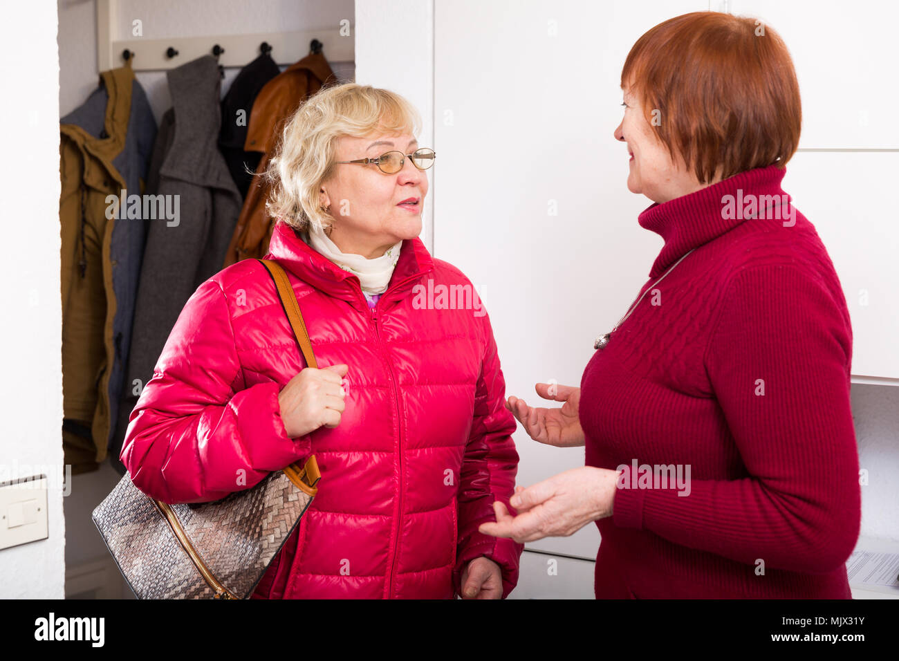 Vieille Femme positive de dire au revoir à un ami femme en veste à l'intérieur Banque D'Images