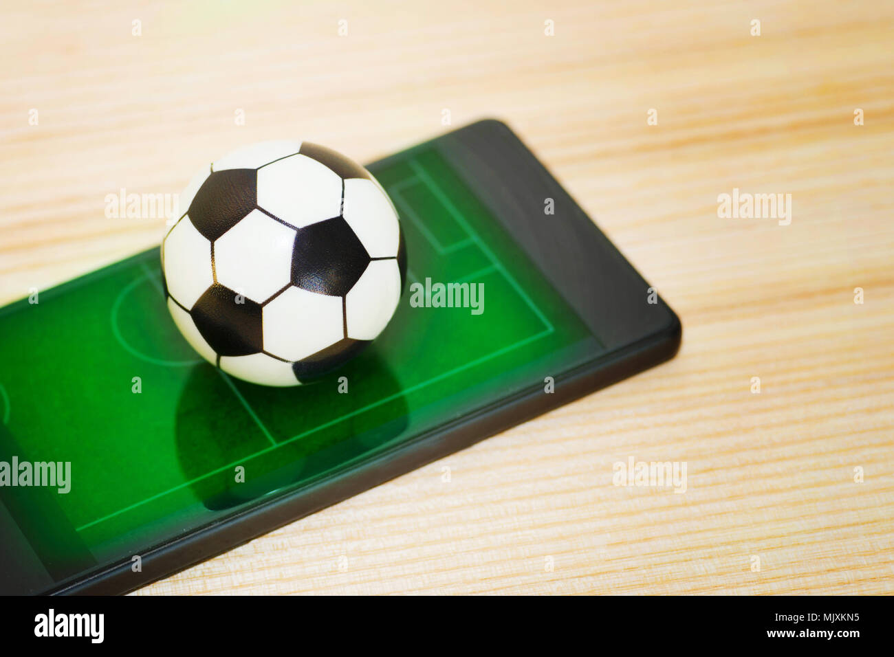 Un jouet ballon de soccer sur un smartphone avec l'image d'un champ vert. Concept du jeu du football. Banque D'Images