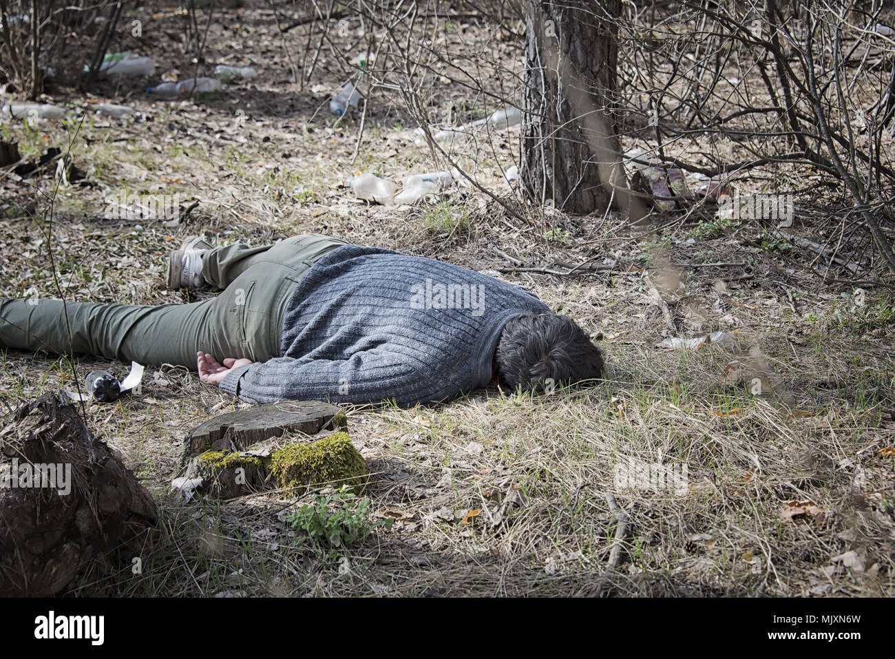 Meurtre dans les bois, un homme mort dans un pull bleu et un pantalon vert allongé sur le sol, au milieu des arbres dans les bois Banque D'Images