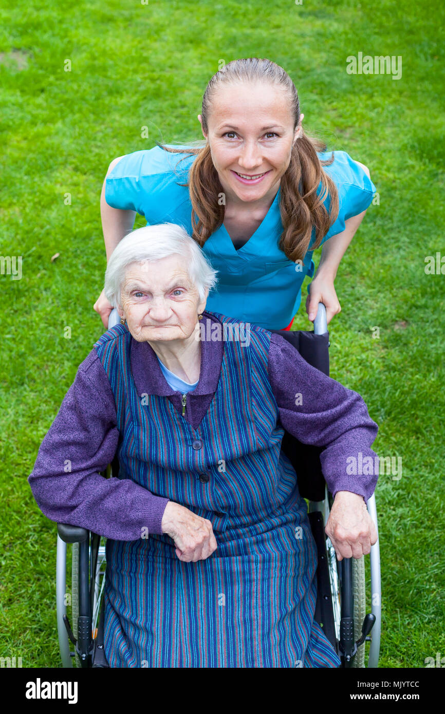 Portrait de personnes âgées handicapées femme assise dans un fauteuil roulant de passer du temps avec l'extérieur cheerful young caregiver Banque D'Images