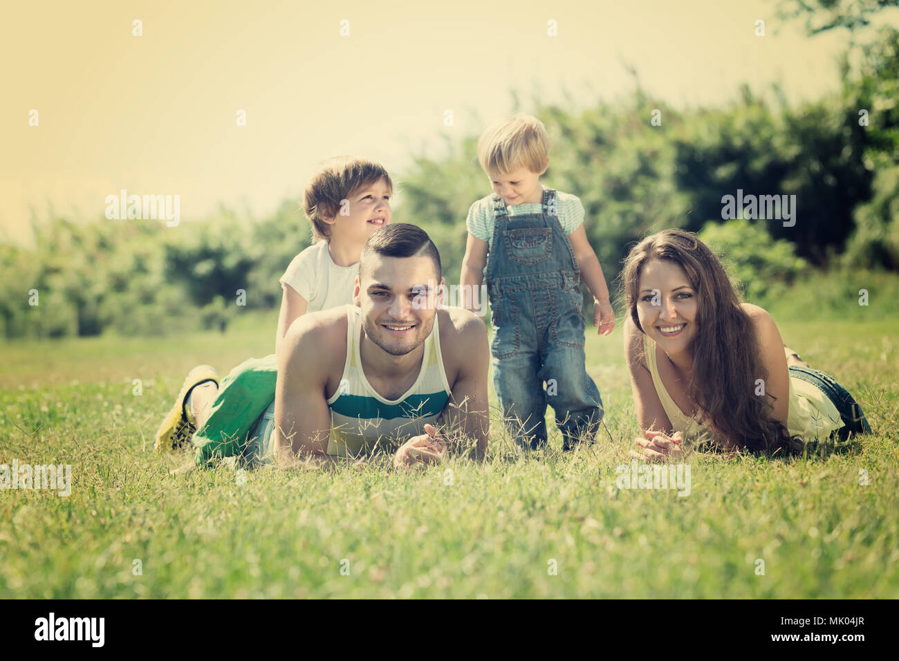 Happy smiling family of four lying on grass in sunny summer park Banque D'Images