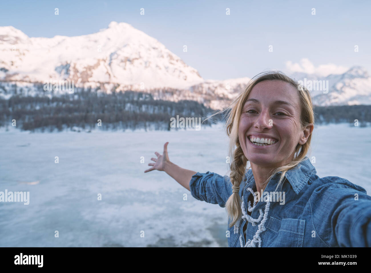 Jeune femme tenant un portrait selfies près d'un lac gelé avec des montagnes aux sommets enneigés en arrière-plan au coucher du soleil. Les gens voyagent fun concept, Suisse. Banque D'Images