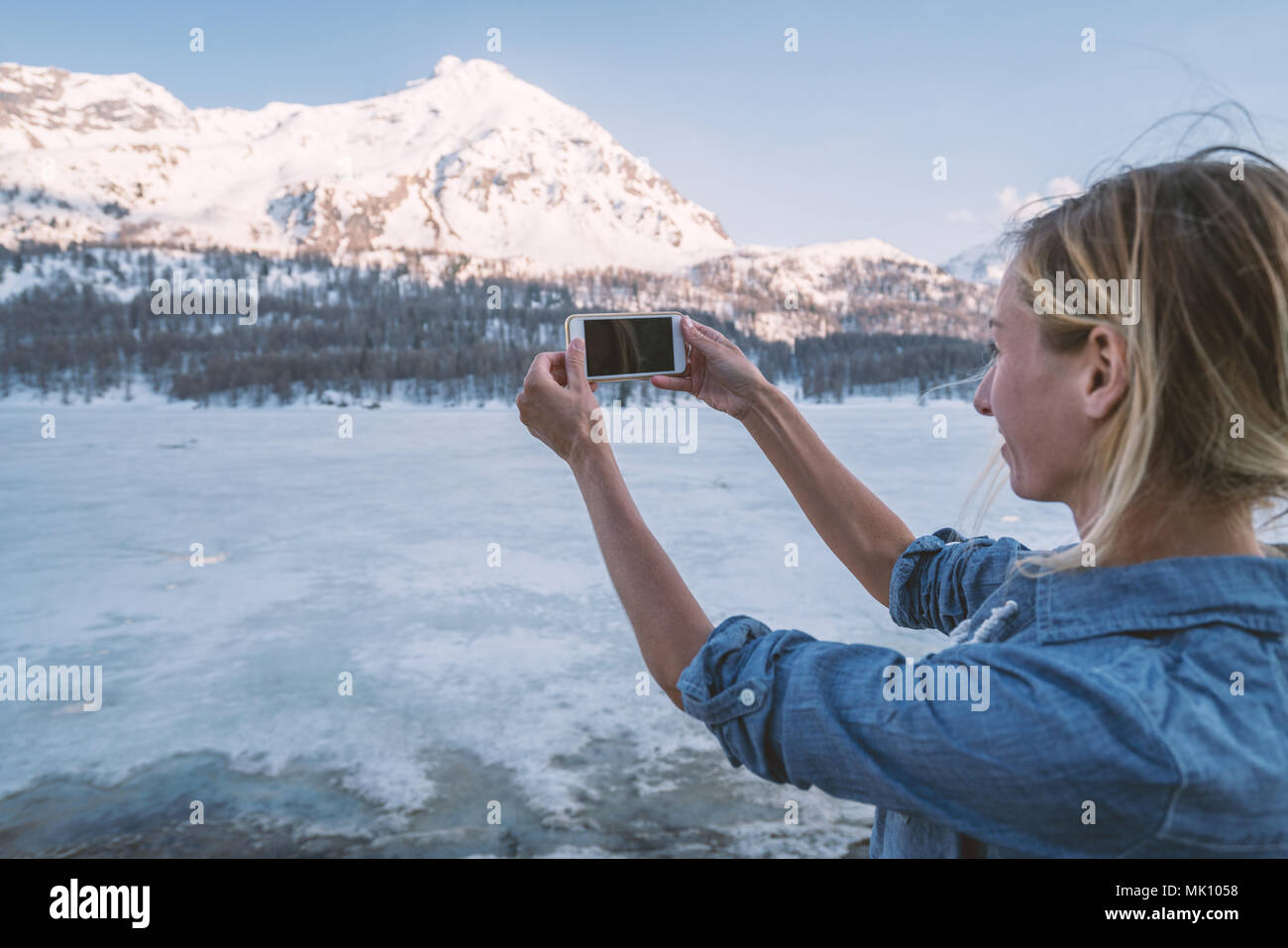 Jeune femme tenant un téléphone mobile photo de magnifiques montagnes au coucher du soleil en Suisse. Les gens voyagent technologie concept Banque D'Images