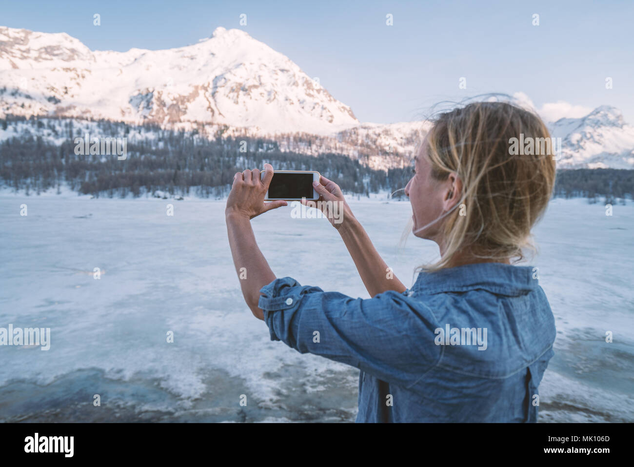 Jeune femme tenant un téléphone mobile photo de magnifiques montagnes au coucher du soleil en Suisse. Les gens voyagent technologie concept Banque D'Images