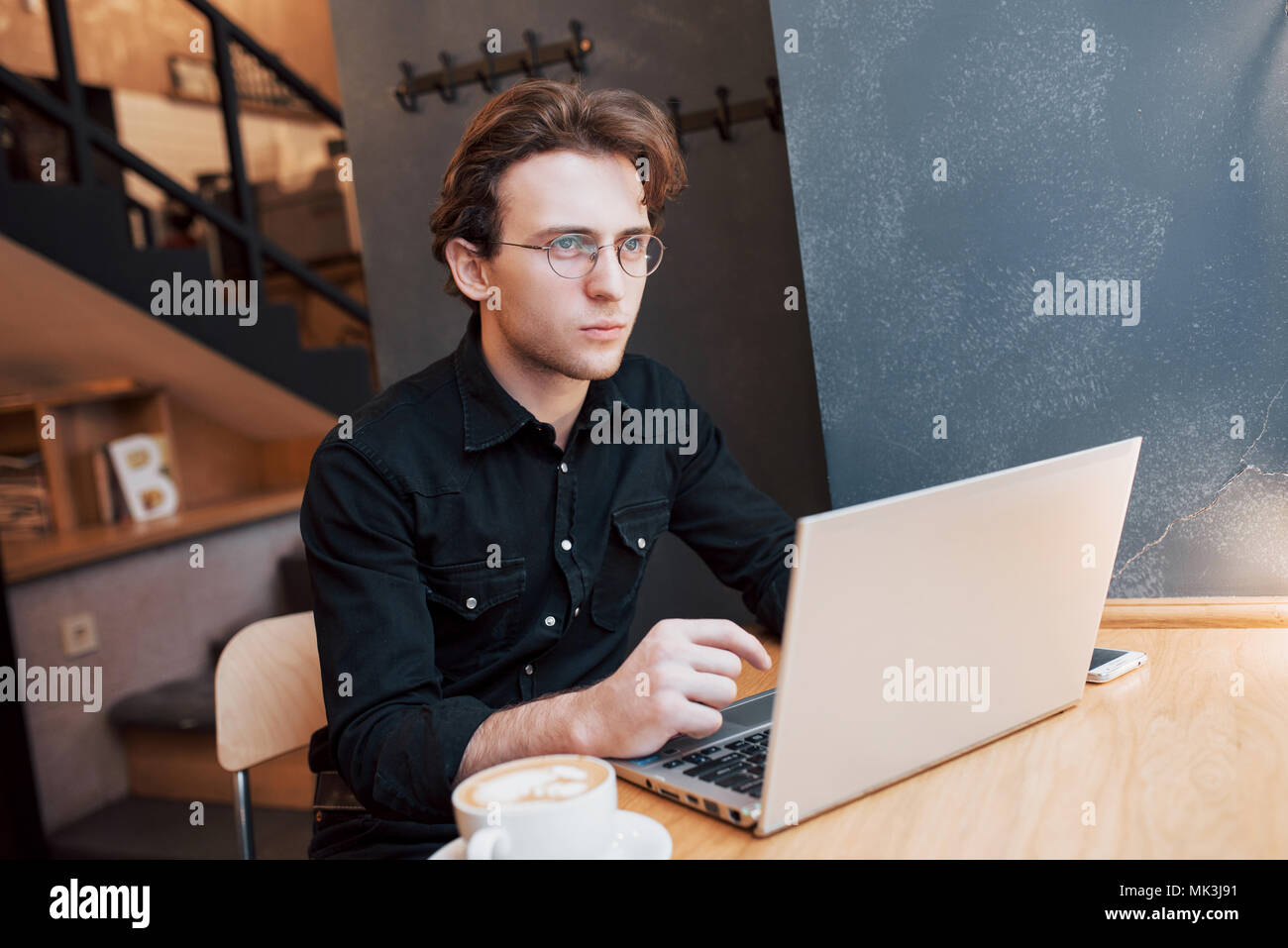 L'homme créatif designer travaillant sur son ordinateur portable lors de l'attente à l'ordre à son favori à l'intérieur, café étudiant travaillant sur le bénéfice net de bord pendant le petit déjeuner du matin au café de l'intérieur moderne Banque D'Images