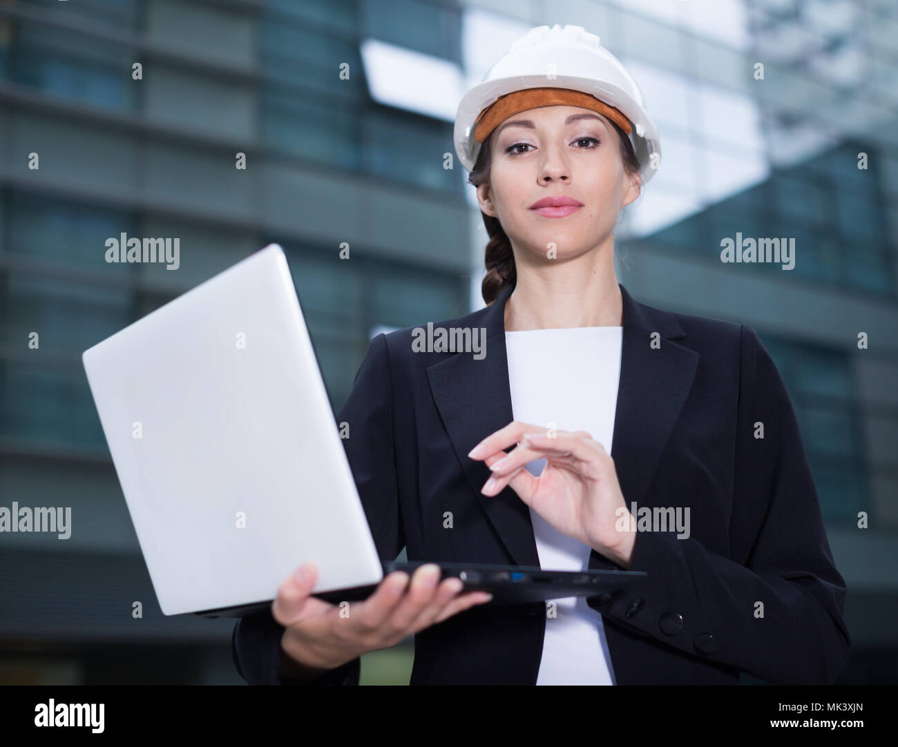 Smiling woman engineer en costume et chapeau avec dossier est l'exploration  de projet dans son ordinateur portable près de l'immeuble Photo Stock -  Alamy