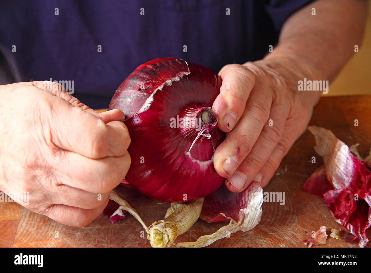 Un homme l'épluchage de la peau externe rugueux d'un gros oignon rouge Banque D'Images