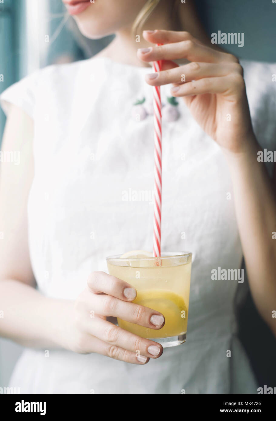 Une femme à boire de la limonade à la femme, en gardant à la main un verre de boisson rafraîchissante avec du citron et de la glace Banque D'Images