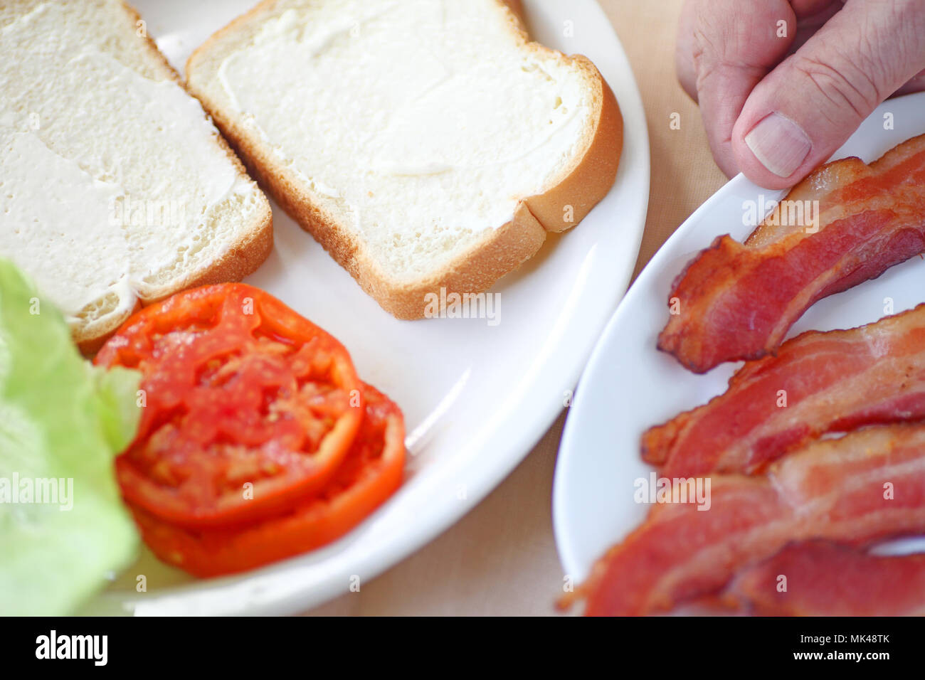 Un homme s'apprête à mettre sur pied un bacon, laitue et tomate sandwich sur pain blanc. Banque D'Images