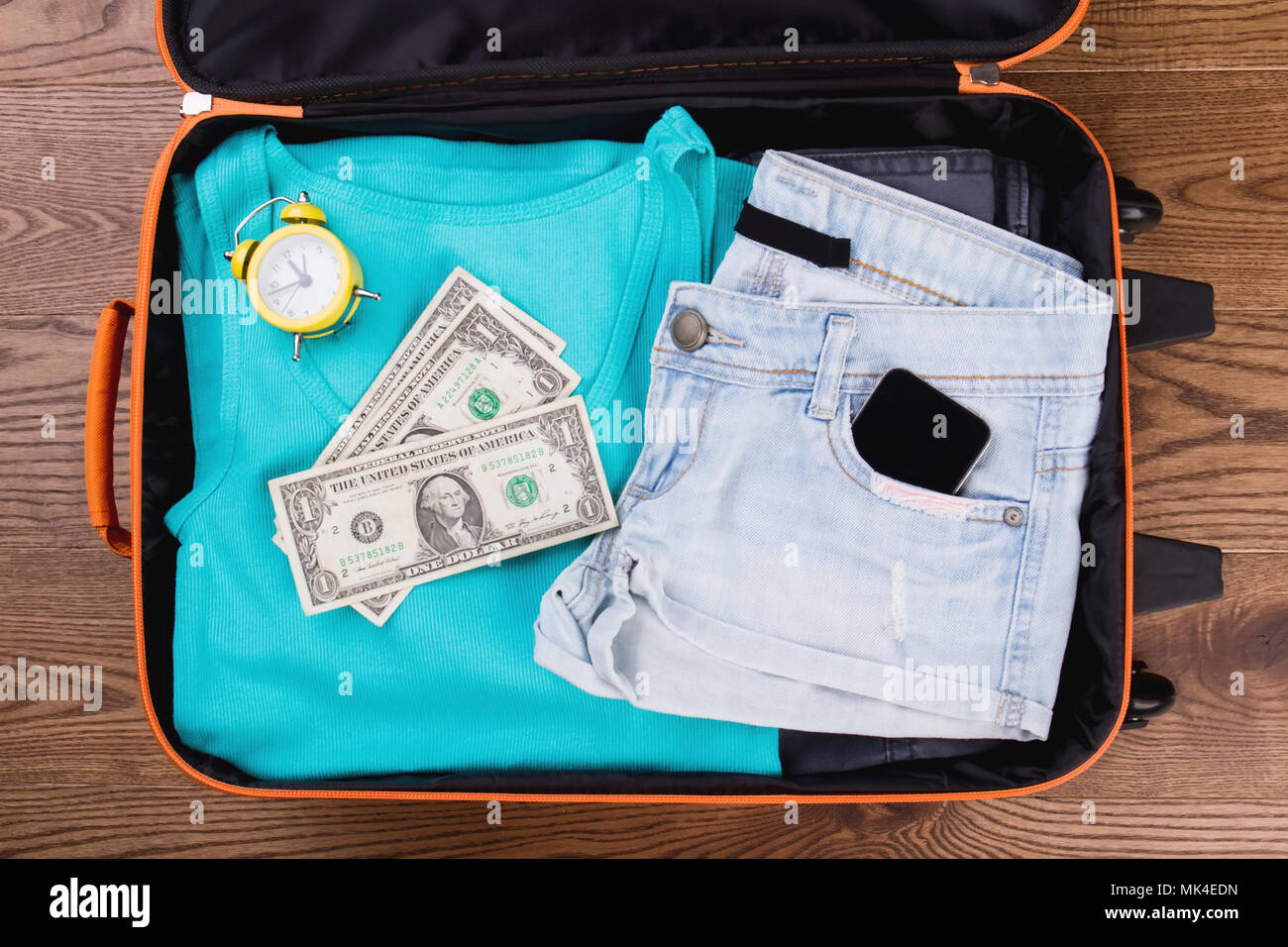 Vêtements femmes d'été et accessoires pour les voyages. Vêtements femme pliée avec réveil et de l'argent dans la valise. Haut de la vue, télévision lay. Banque D'Images