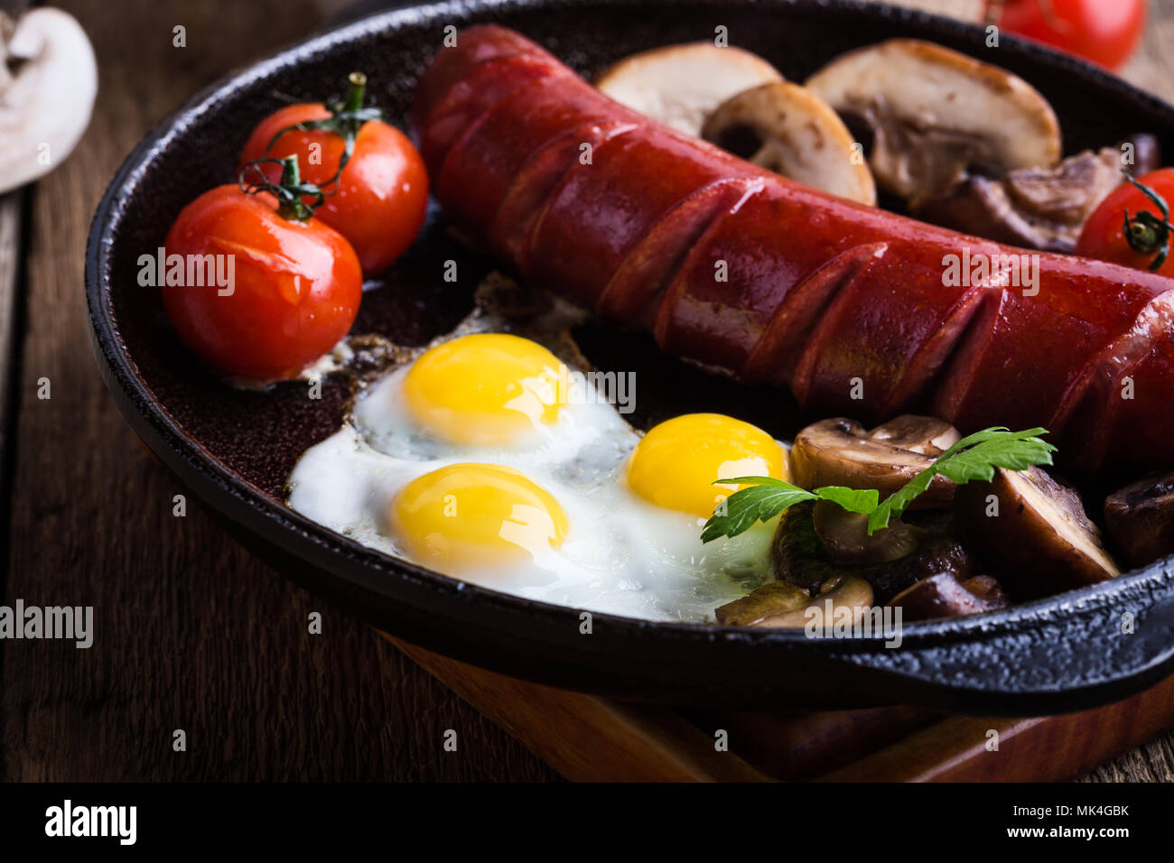Oeufs de caille au plat, saucisses, tomates et champignons sur le poêle en fonte, petit déjeuner anglais style rustique Banque D'Images