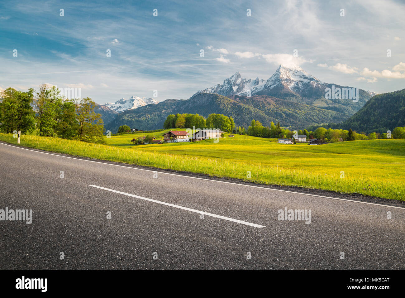 Vue panoramique de empty country road menant à travers les magnifiques paysages de montagne alpin avec des prés verts plein de fleurs au printemps Banque D'Images