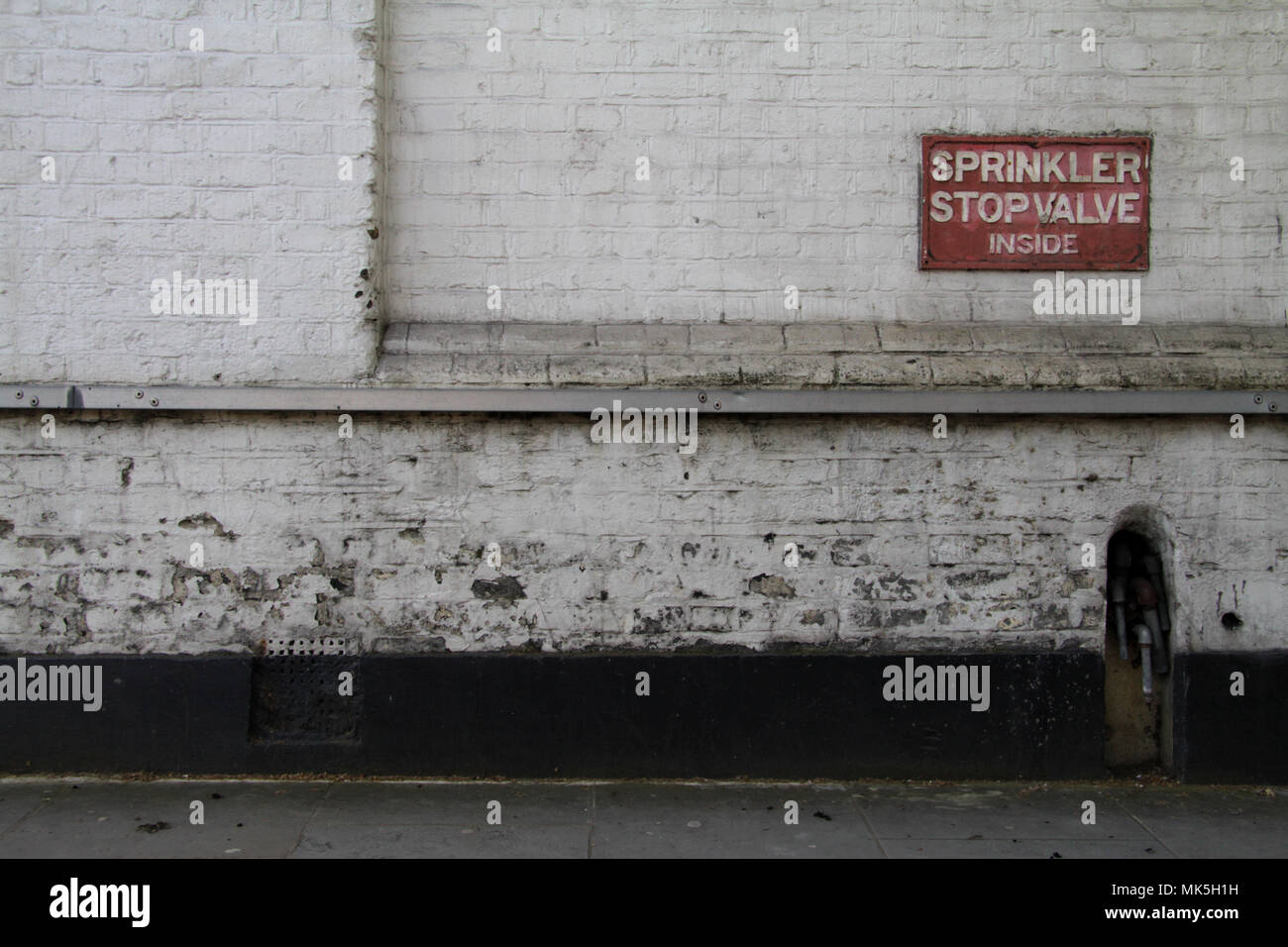 Le clapet d'arrêt sprinkleur signe sur un mur de brique briques peints en blanc Banque D'Images