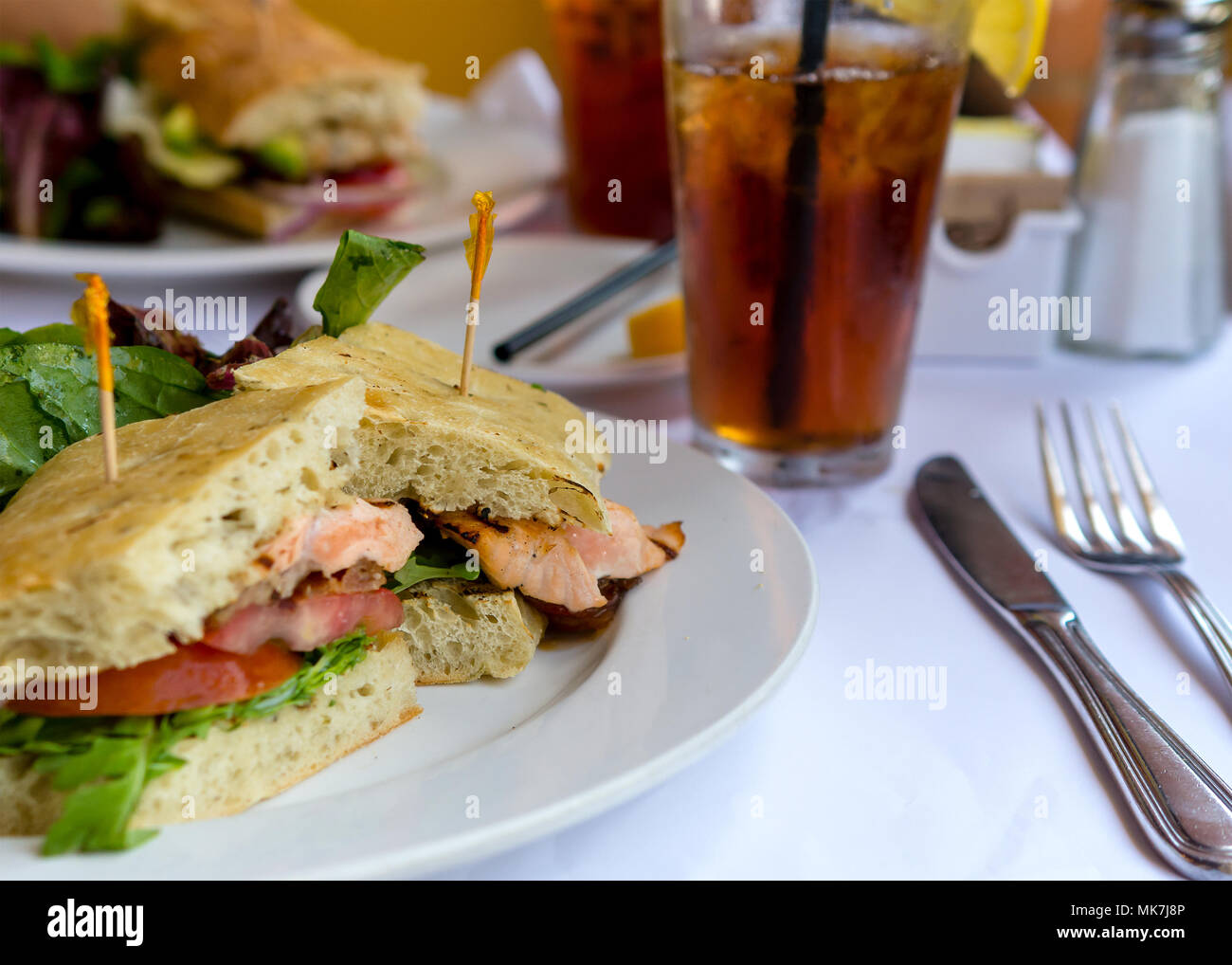 Gros plan sur le saumon grillé sandwich au pain ciabatta blanc nappe sur la plaque et dans le cadre d'un restaurant accompagné de thé glacé Banque D'Images