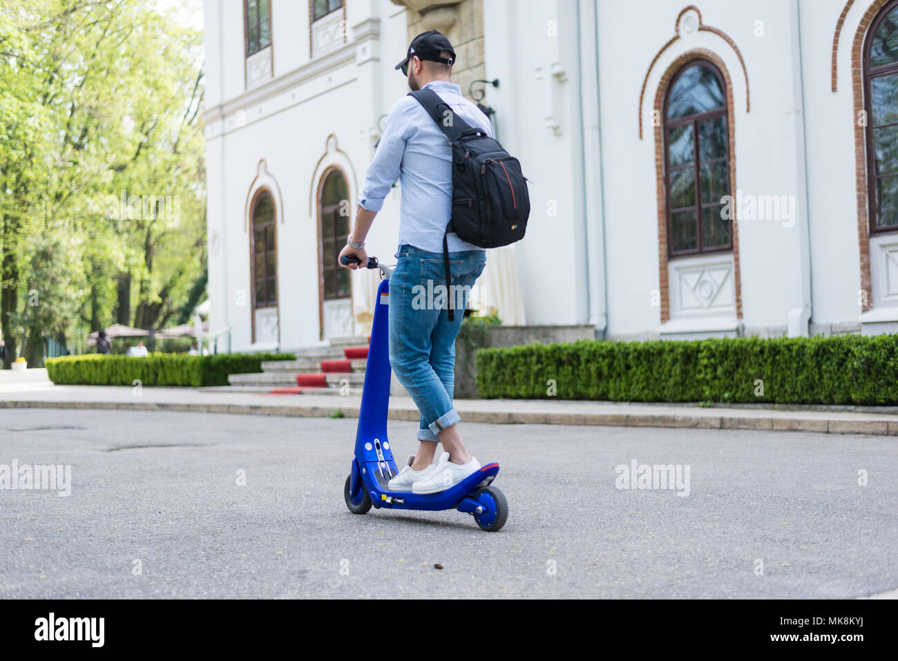Personne à l'aide de scooter électrique et une smartwatch dans le parc et dans la rue, lors d'une journée ensoleillée, avec effet de flou. Banque D'Images