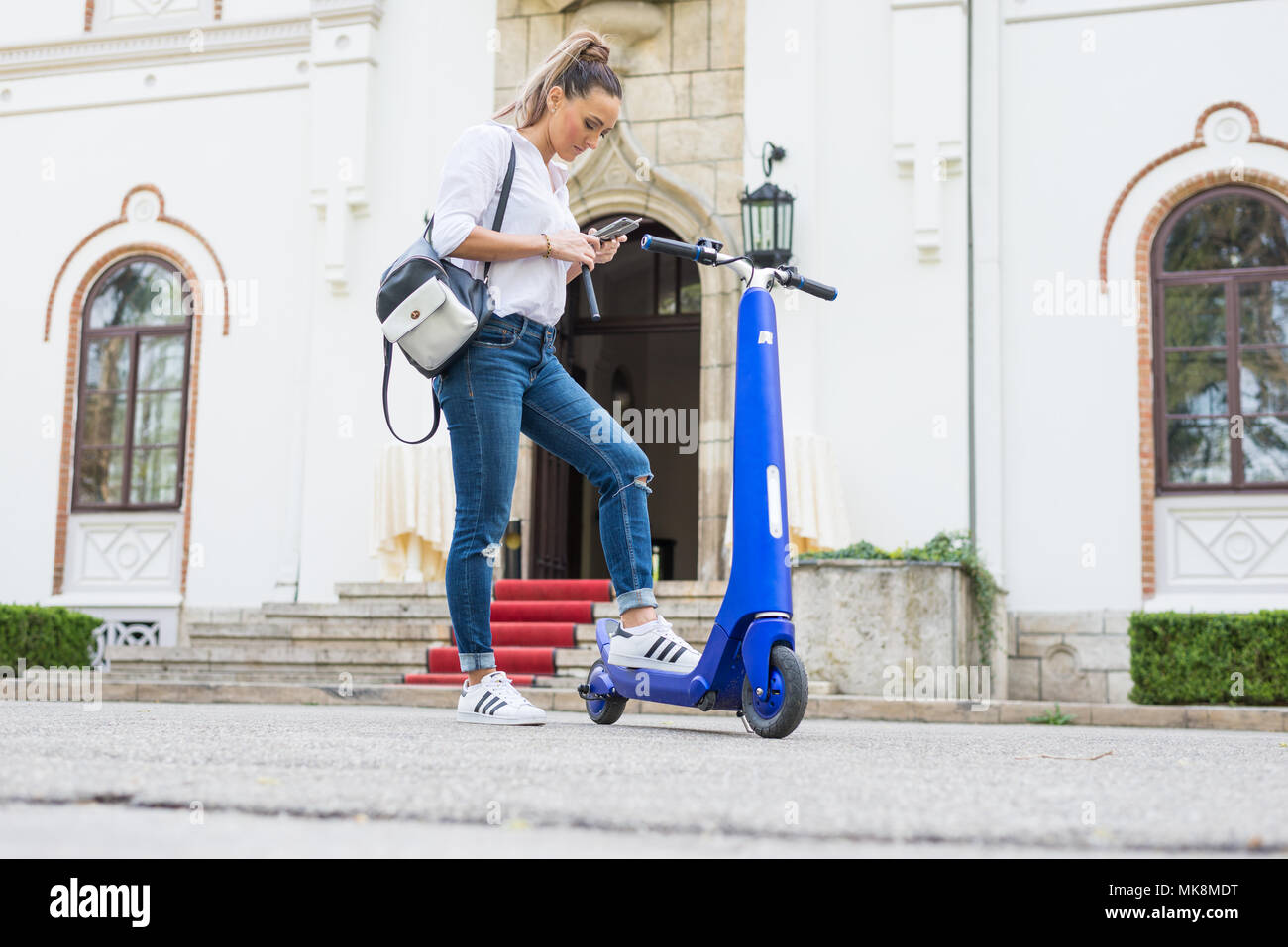 Personne à l'aide de scooter électrique et une smartwatch dans le parc et dans la rue, lors d'une journée ensoleillée, avec effet de flou. Banque D'Images