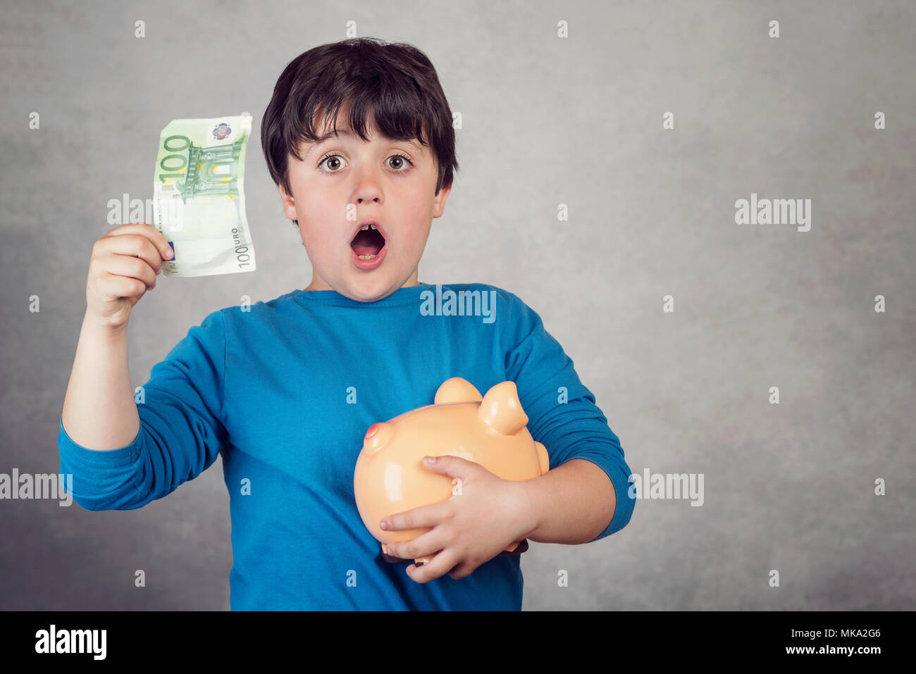 L'enfant surpris d'économiser de l'argent dans une tirelire sur fond gris Banque D'Images