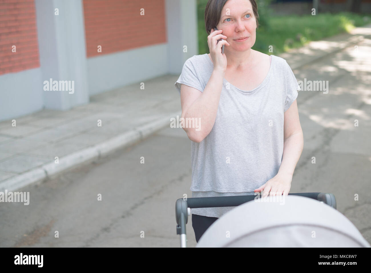 Happy mother talking on mobile phone et en poussant bébé dans une poussette en marchant sur la rue en vêtements de sport décontracté Banque D'Images