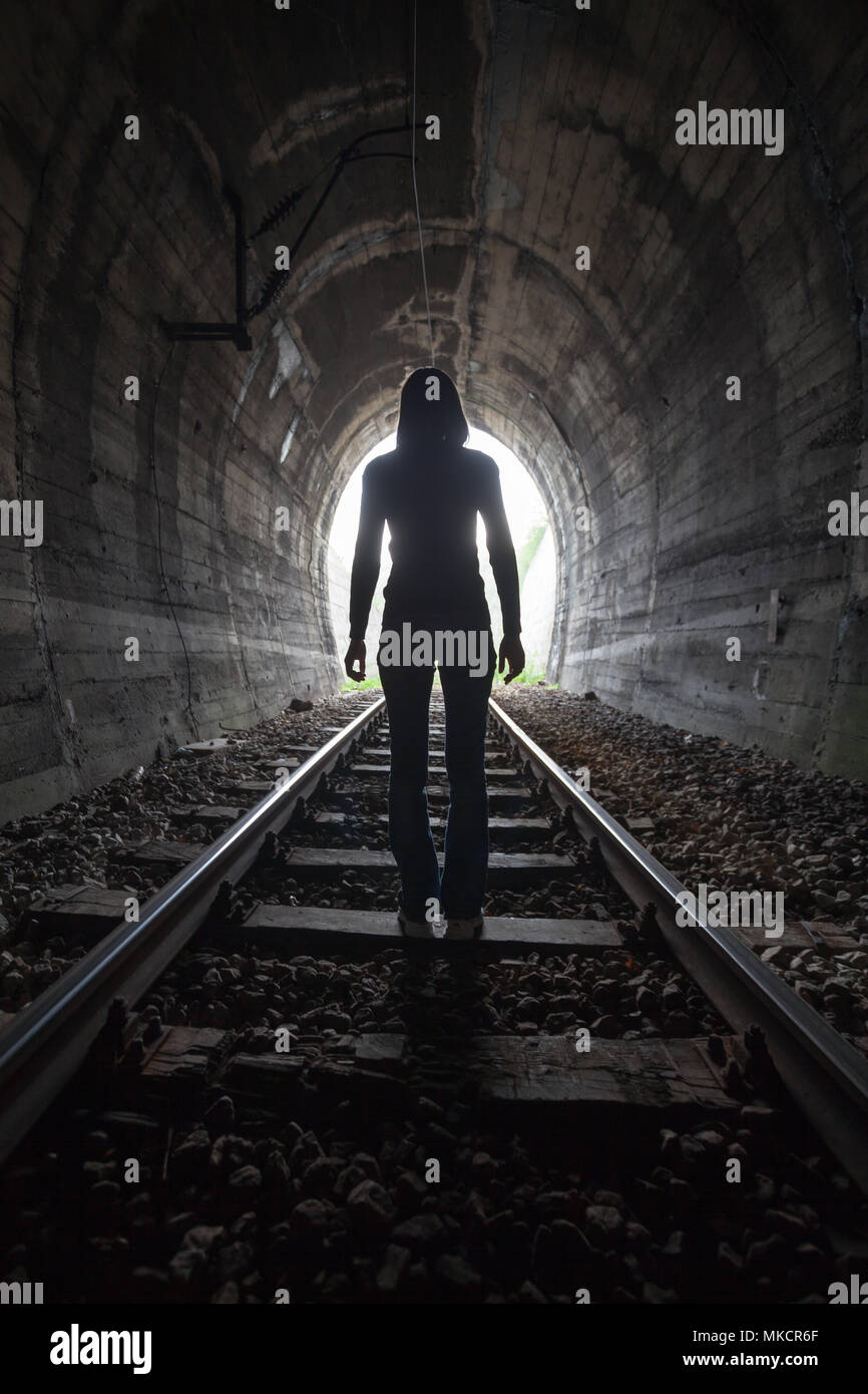 L'homme qui se profile dans un tunnel debout au milieu de la voie ferrée à la recherche vers la lumière au bout du tunnel dans une image conceptuelle Banque D'Images